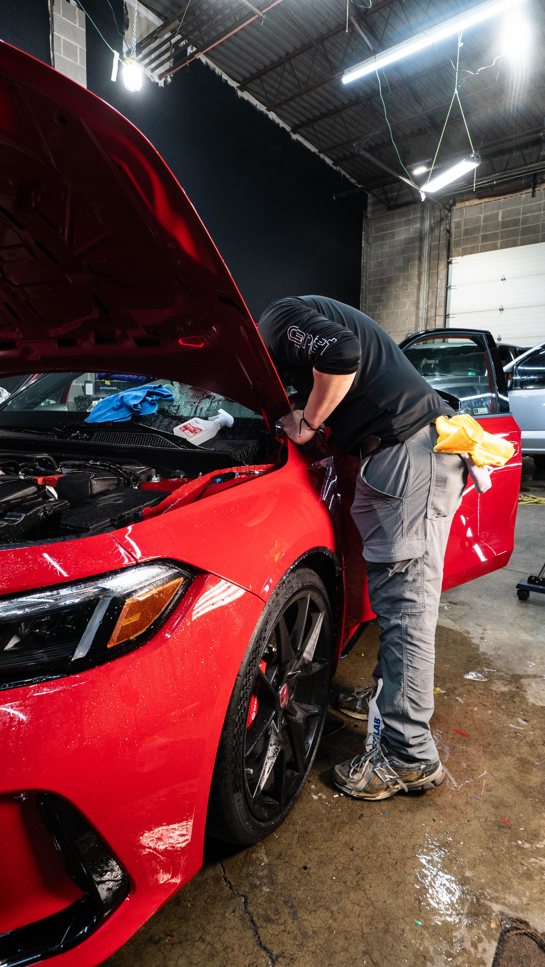 Skyline Customs technician working on a red vehicle with the hood open inside the Chantilly shop
